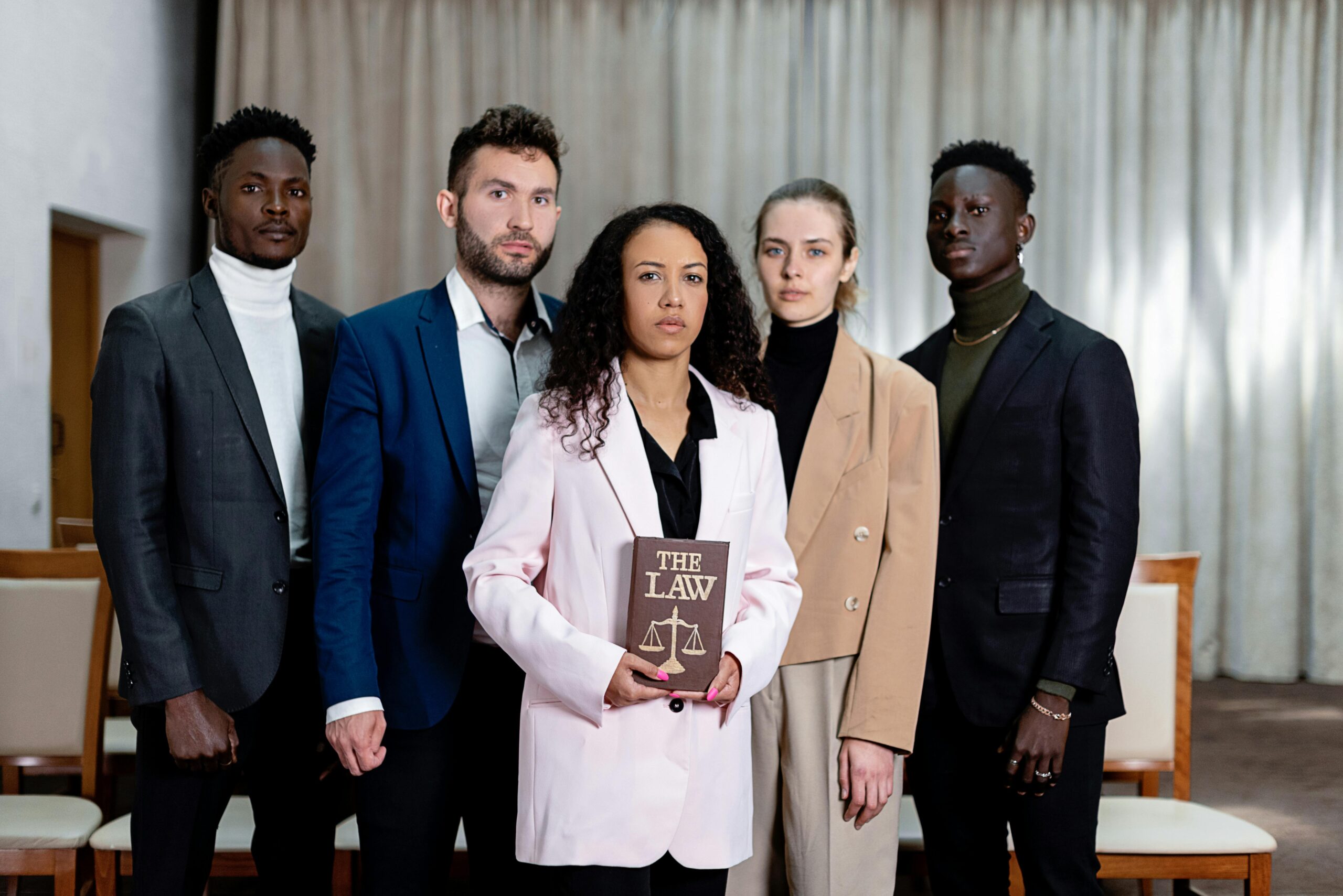 A diverse group of five lawyers posing confidently with a law book in an office setting.
